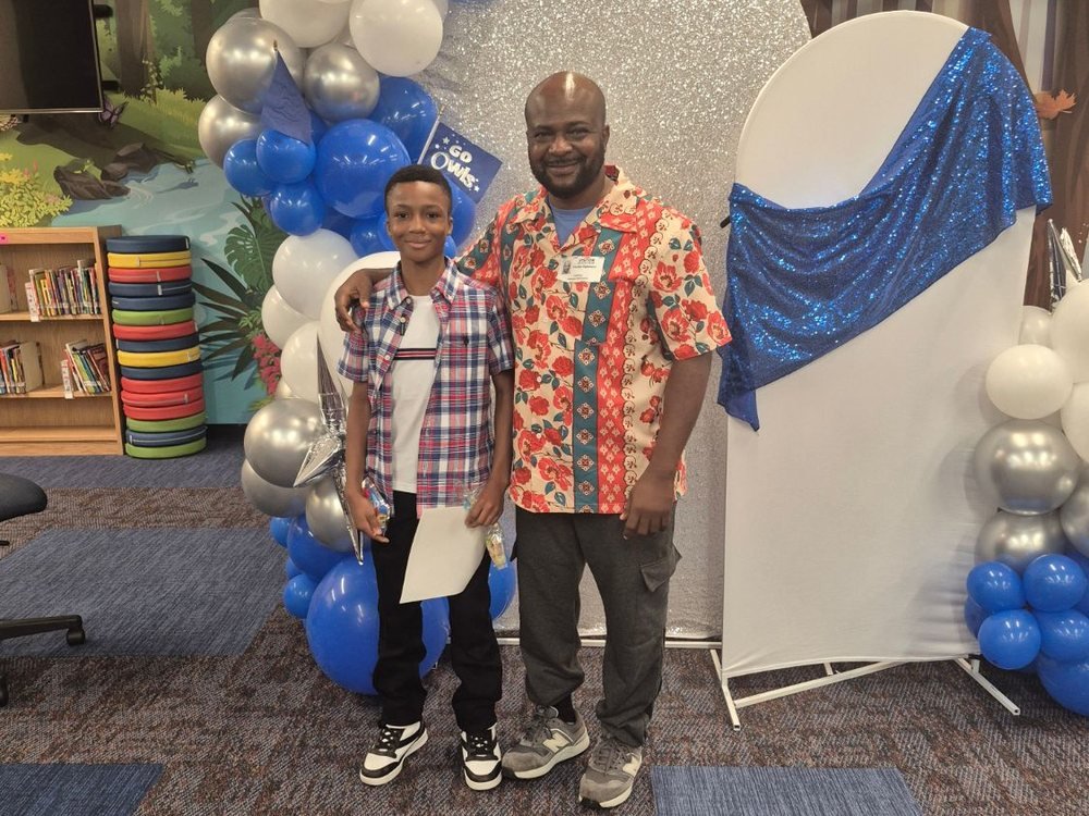 Emeka Ogbonna with family at a school celebration, standing in front of blue and white balloons